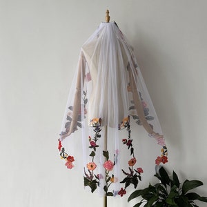 May include: White bridal veil with floral embroidery. The veil is made of tulle and features a variety of colourful flowers, including red, orange, yellow, pink and purple.