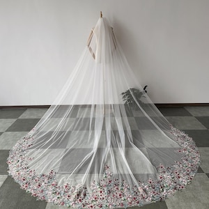 May include: A long, white tulle wedding veil with a floral embroidered border. The embroidery features pink, red, and green flowers.