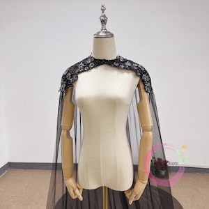 Peut inclure: Une cape noire en tulle avec une bordure noire en sequins. La cape est drapée sur un mannequin.