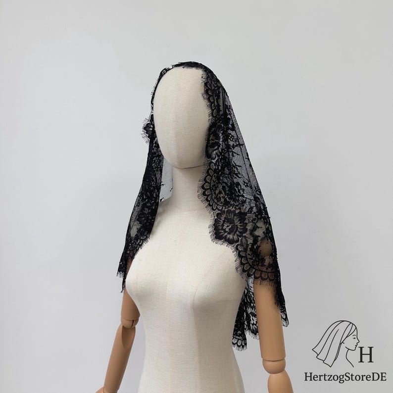 Peut inclure: Un voile en dentelle noire avec un motif floral et des bords festonn&eacute;s est drap&eacute; sur un mannequin. Le voile est fait d'un tissu d&eacute;licat et transparent et est con&ccedil;u pour &ecirc;tre port&eacute; sur la t&ecirc;te et les &eacute;paules.