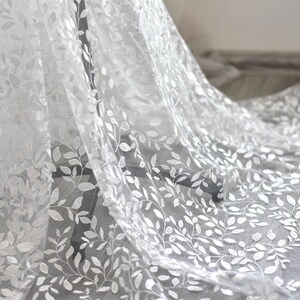 May include: White sheer fabric with an embroidered leaf pattern. The fabric is delicate and has a soft, flowing texture.