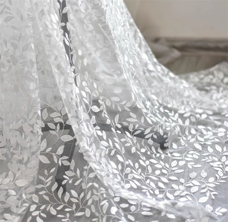 May include: White sheer fabric with an embroidered leaf pattern. The fabric is delicate and has a soft, flowing texture.