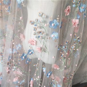 May include: Pale pink tulle fabric with embroidered blue and pink flowers. The fabric has a delicate, feminine look and would be perfect for a variety of projects.