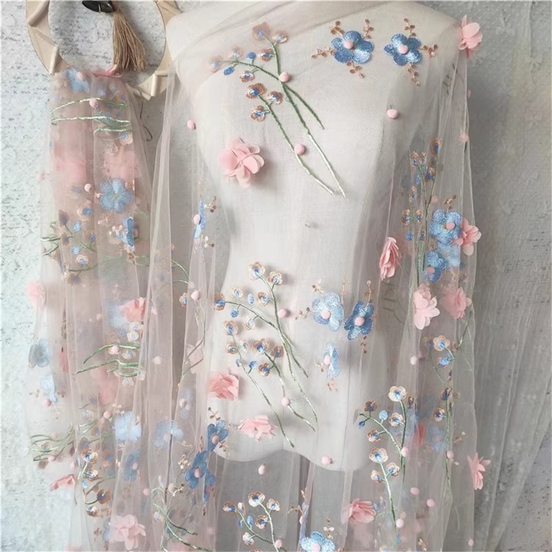 May include: Pink sheer fabric with blue and pink embroidered flowers. The fabric has a delicate, feminine look and would be perfect for a variety of crafting projects.