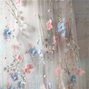 May include: Pale pink and light blue floral embroidery on a sheer white tulle fabric. The flowers are 3D and have a delicate, feminine look.