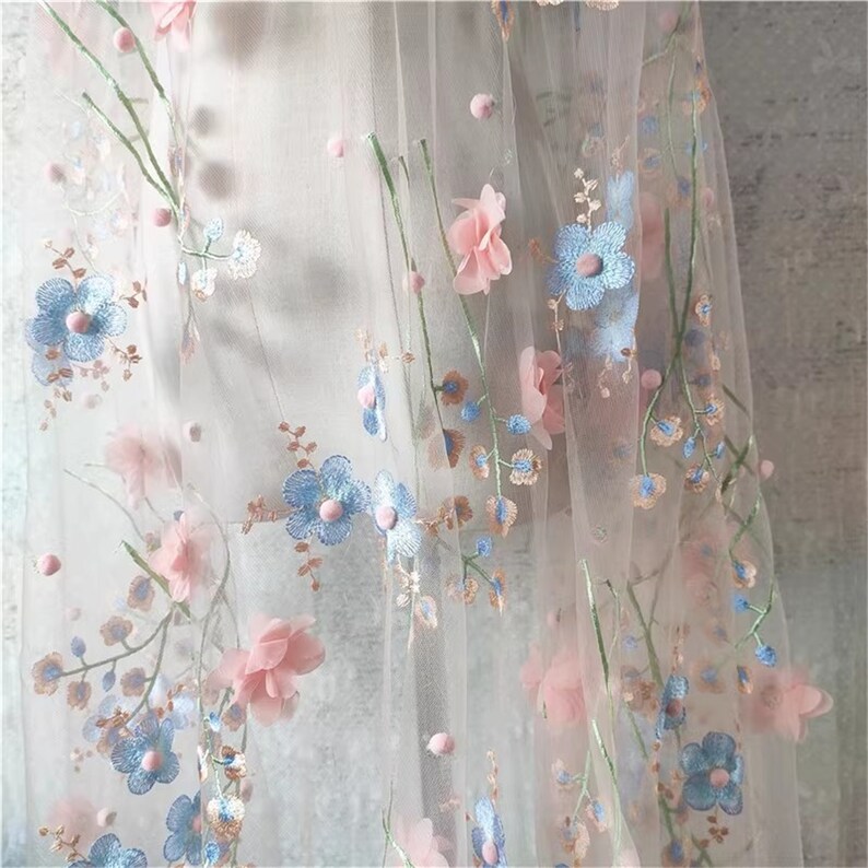 May include: Pale pink and light blue floral embroidery on a sheer white tulle fabric. The flowers are 3D and have a delicate, feminine look.