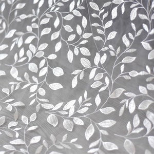 May include: White embroidered tulle fabric with a delicate leaf pattern. The fabric is sheer and lightweight, making it ideal for a variety of crafting projects.