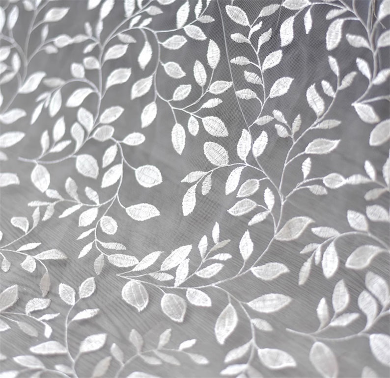 May include: White embroidered tulle fabric with a delicate leaf pattern. The fabric is sheer and lightweight, making it ideal for a variety of crafting projects.