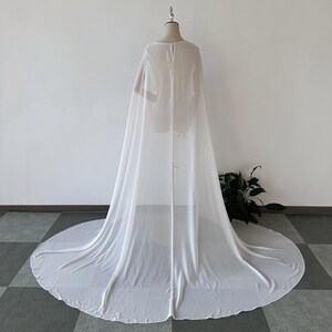K&ouml;nnte beinhalten: Ein wei&szlig;er, durchsichtiger Chiffon-Umhang mit langem Schleier. Der Umhang ist &uuml;ber eine Kleiderpuppe gelegt und hat ein schlichtes, elegantes Design.