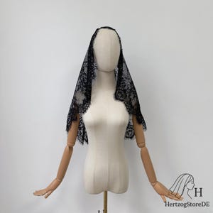 Peut inclure: Un voile en dentelle noire avec un motif floral est drap&eacute; sur un mannequin. Le voile a un bord festonn&eacute; et est pr&eacute;sent&eacute; sur un fond blanc. Le mannequin a des bras articul&eacute;s en bois.