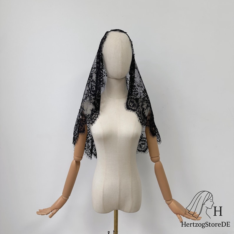 Peut inclure: Un voile en dentelle noire avec un motif floral est drap&eacute; sur un mannequin. Le voile a un bord festonn&eacute; et est pr&eacute;sent&eacute; sur un fond blanc. Le mannequin a des bras articul&eacute;s en bois.
