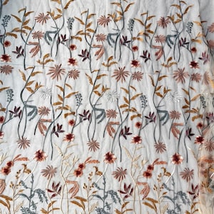 May include: Sheer white fabric with embroidered floral design. The embroidery features a repeating pattern of stylized flowers and leaves in shades of brown, red, gray, and white. The fabric is lightweight and delicate.
