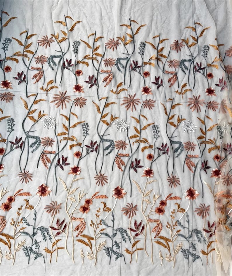 May include: Sheer white fabric with embroidered floral design. The embroidery features a repeating pattern of stylized flowers and leaves in shades of brown, red, gray, and white. The fabric is lightweight and delicate.