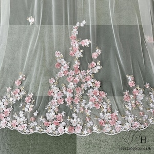 May include: Sheer white fabric with embroidered pink and white floral design. The delicate flowers are clustered along the bottom edge and scattered across the fabric. The fabric has a scalloped edge.