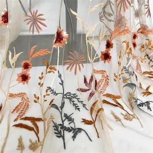 May include: Sheer fabric with embroidered floral design. The embroidery features flowers and foliage in shades of brown, orange, and gray against a beige background. The fabric is lightweight and delicate, suitable for curtains or decorative purposes.