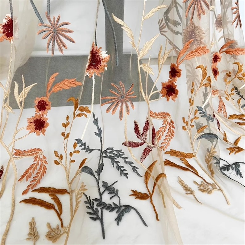 May include: Sheer fabric with embroidered floral design. The embroidery features flowers and foliage in shades of brown, orange, and gray against a beige background. The fabric is lightweight and delicate, suitable for curtains or decorative purposes.