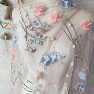 May include: Pale pink tulle fabric with embroidered blue and pink flowers and small white pom-poms.