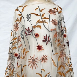 May include: Sheer fabric with embroidered floral design. The embroidery features flowers and leaves in shades of brown, orange, and burgundy. The fabric is a light beige color, and the floral design is spread across the material.