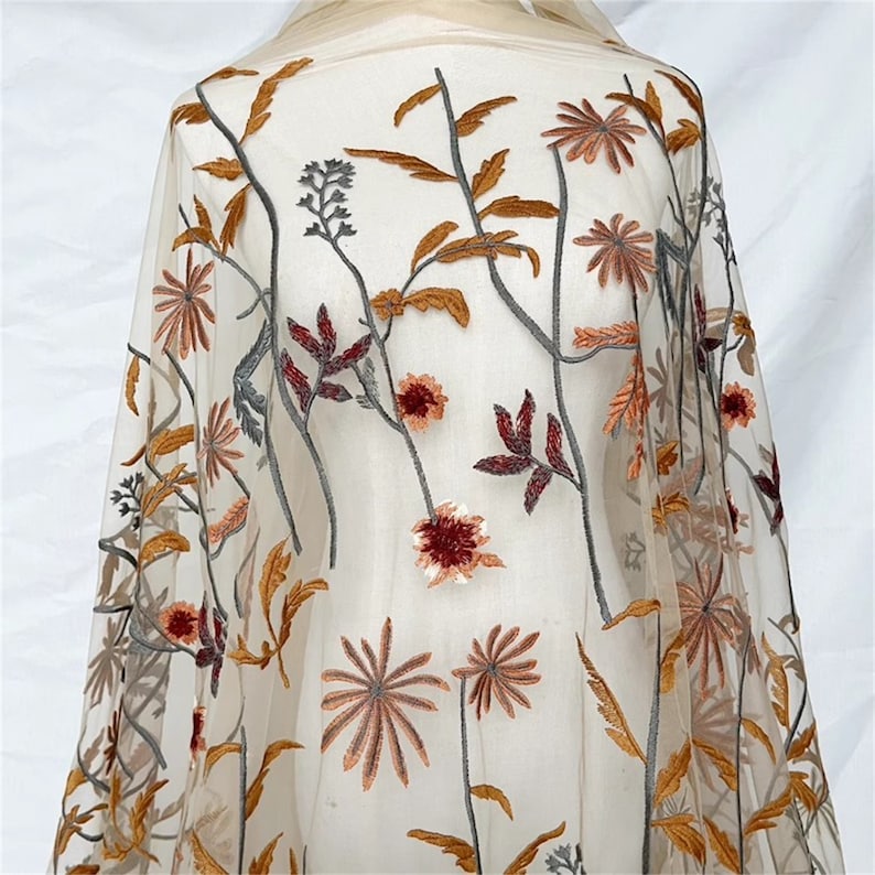 May include: Sheer fabric with embroidered floral design. The embroidery features flowers and leaves in shades of brown, orange, and burgundy. The fabric is a light beige color, and the floral design is spread across the material.