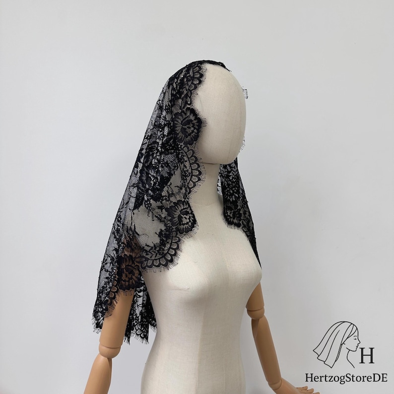 Peut inclure: Voile en dentelle noire avec un motif floral et des bords festonn&eacute;s. Le voile est drap&eacute; sur un mannequin, mettant en valeur son design d&eacute;licat et sa texture. Un accessoire traditionnel souvent utilis&eacute; pour les c&eacute;r&eacute;monies religieuses ou les occasions sp&eacute;ciales.