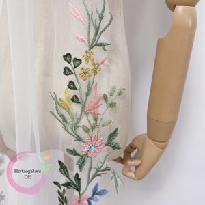 K&ouml;nnte beinhalten: Wei&szlig;er T&uuml;llstoff mit gesticktem Blumenmuster in Rosa, Gr&uuml;n, Gelb und Blau. Die Stickerei zeigt Blumen, Bl&auml;tter und Stiele.