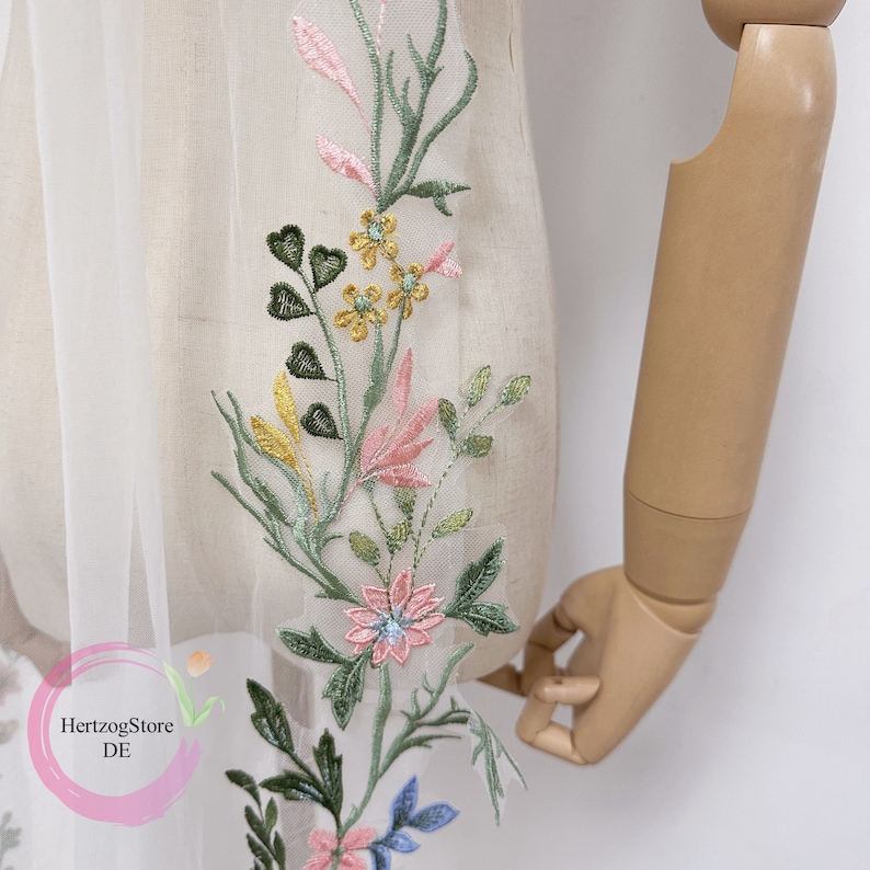 K&ouml;nnte beinhalten: Wei&szlig;er T&uuml;llstoff mit gesticktem Blumenmuster in Rosa, Gr&uuml;n, Gelb und Blau. Die Stickerei zeigt Blumen, Bl&auml;tter und Stiele.
