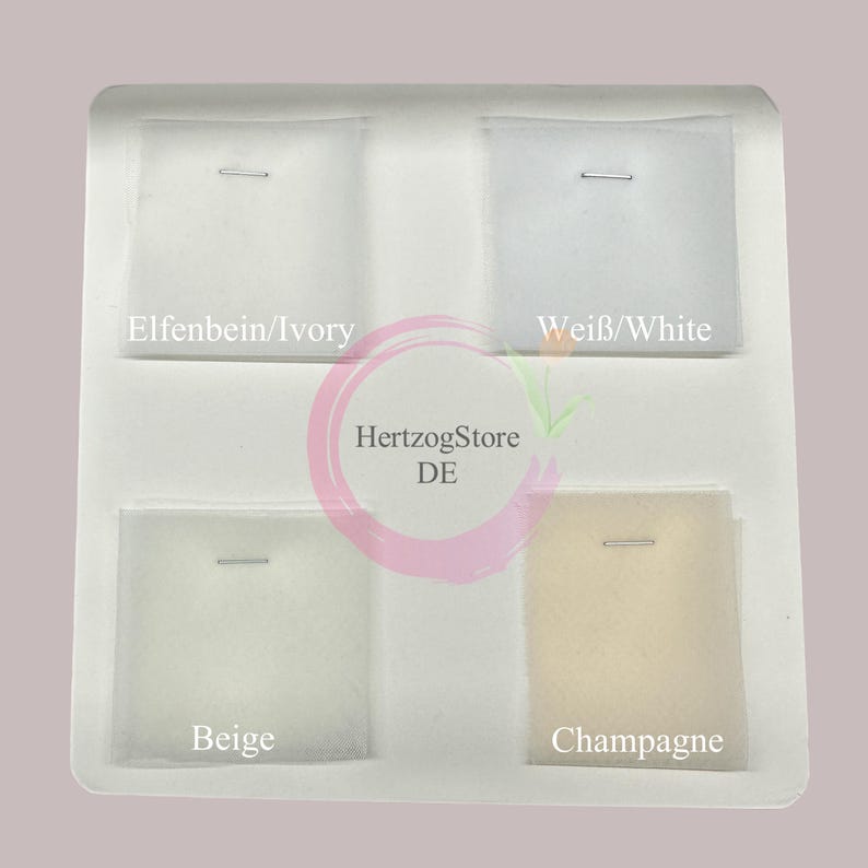 May include: A display of fabric swatches in ivory, white, beige, and champagne colors, each secured with a metal staple. The swatches are arranged in a white tray, with text labels indicating the color names.