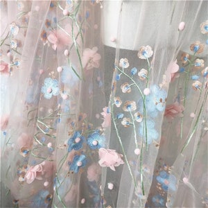 May include: Pink and blue floral embroidered tulle fabric with 3D flowers. The fabric has a delicate, sheer texture and is perfect for crafting and sewing projects.