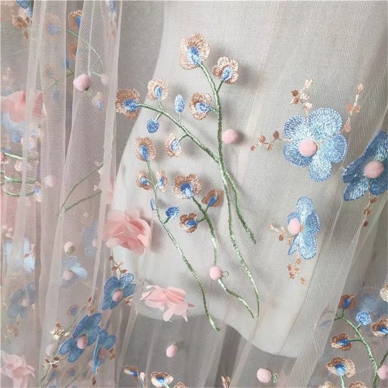 May include: Pink and blue floral embroidered tulle fabric with small white pom-poms.