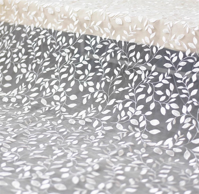 May include: White sheer fabric with an embroidered leaf pattern. The fabric is delicate and has a soft, flowing texture.