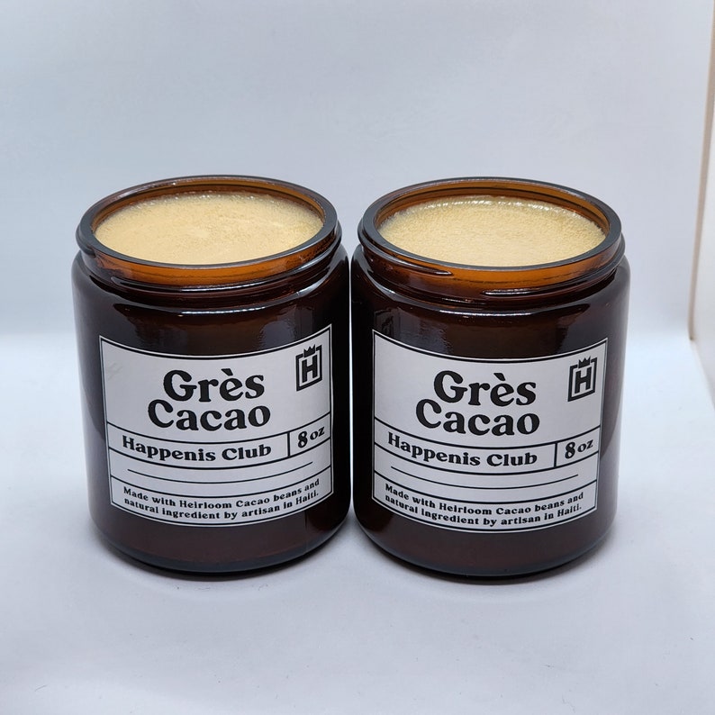 Peut inclure: Deux pots en verre brun avec des &eacute;tiquettes blanches. Les &eacute;tiquettes indiquent "Gr&egrave;s Cacao Happenis Club 8 oz" et "Fabriqu&eacute; avec des f&egrave;ves de cacao anciennes et des ingr&eacute;dients naturels par un artisan en Ha&iuml;ti".