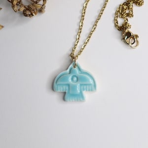 May include: A gold chain necklace featuring a light blue bird-shaped pendant. The pendant has a detailed design and is the focal point of the necklace. The necklace is presented on a white surface.