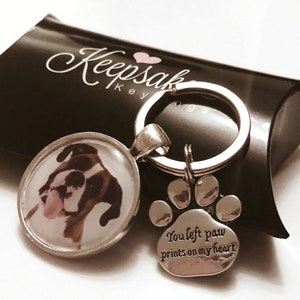 May include: Silver keyring with a photo of a boxer dog in a round glass charm and a paw print charm with the text "You left paw prints on my heart".
