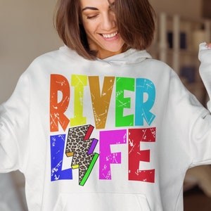 以下が含まれることがあります： 「River Life」と雷とヒョウ柄のデザインが施された、虹色のグラフィックがプリントされた白いパーカー