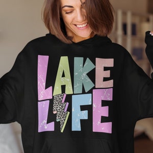 以下が含まれることがあります： レトロなスタイルで「LAKE LIFE」と書かれたカラフルなグラフィックが施された黒いパーカー。グラフィックには稲妻とヒョウ柄のパターンが描かれています。