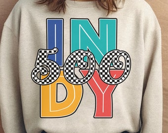 May include: Beige sweatshirt with the word "INDY 500" in a colorful, retro design. The "IN" is blue and teal, the "500" is black and white checkered, and the "DY" is yellow and red.