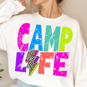 以下が含まれることがあります： 「CAMP LIFE」と雷とヒョウ柄のデザインが施されたカラフルなグラフィックプリントの白いスウェットシャツです。