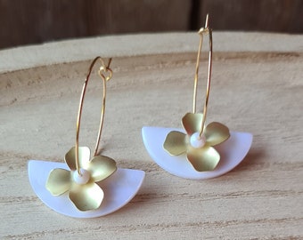 May include: Gold hoop earrings with a white half-circle and a gold flower charm. The flower has a white pearl in the center.