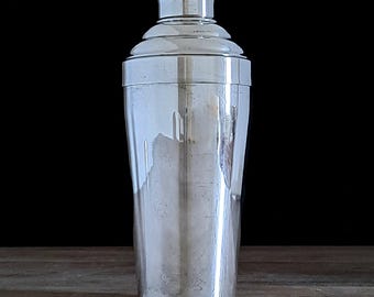 Puede incluir: Una coctelera de plata con cuerpo acanalado y tapa decorativa.