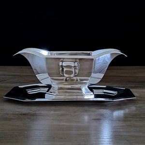 Peut inclure: Un saucier en argent avec une base carrée et une poignée décorative. Le saucier est posé sur un plateau en argent assorti.