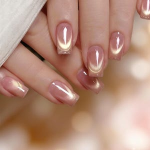 Puede incluir: Primer plano de una mano con uñas manicuradas. Las uñas son de un rosa suave con un efecto brillante de ojo de gato en dorado. Las uñas son de forma cuadrada y tienen un acabado brillante, creando un aspecto sofisticado y elegante.