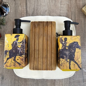 May include: Two yellow and black soap dispensers with a wooden soap dish. The dispensers feature a design of a person riding a horse.