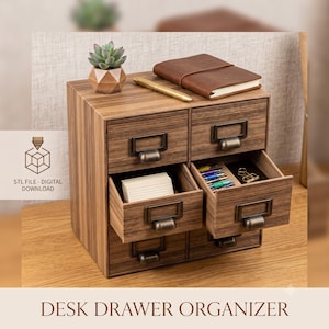 Puede incluir: Un organizador de escritorio de madera con cuatro cajones, acabado de veta de madera y tiradores de metal en tono latón antiguo. Dos cajones están abiertos, revelando un montón de tarjetas blancas y una colección de bolígrafos con un clip.
