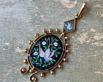 May include: A gold pendant featuring a black and green mosaic depicting two birds in flight. The pendant is surrounded by gold beads and has a smaller diamond-shaped mosaic with a single bird on top.