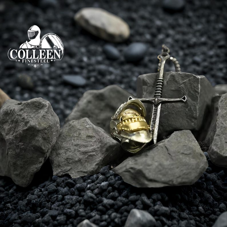 May include: A silver and gold pendant necklace featuring a sword and helmet design. The pendant is on a black background with rocks.