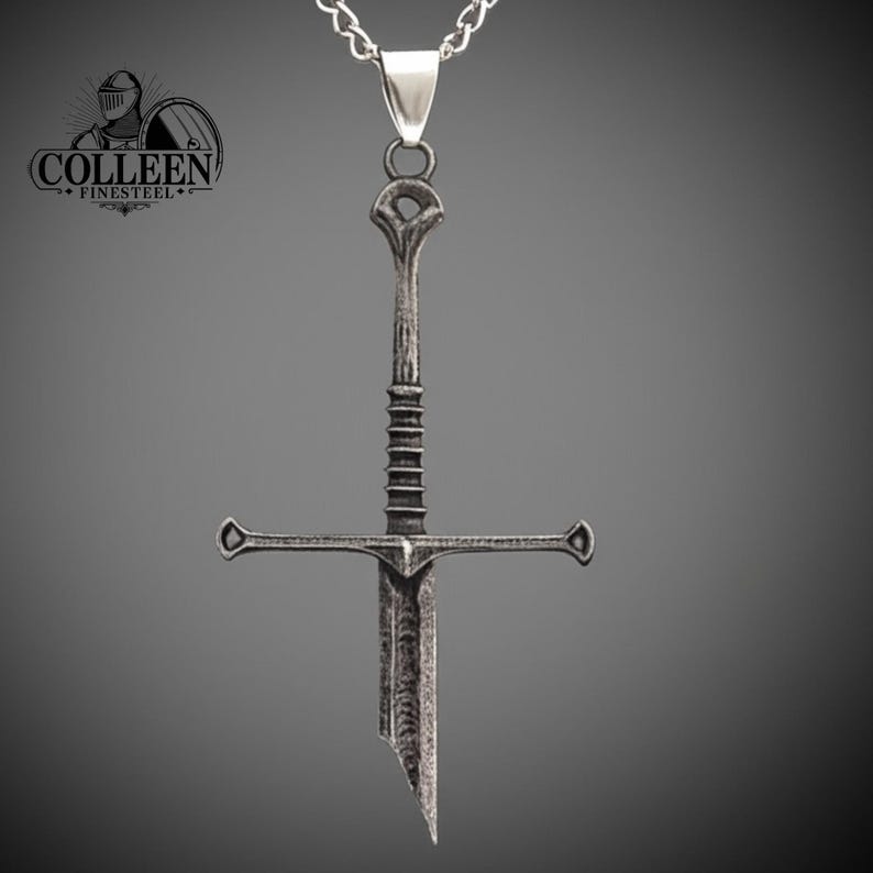 May include: A silver sword pendant necklace with a detailed design. The sword has a cross guard and a pointed tip. The necklace is on a silver chain.