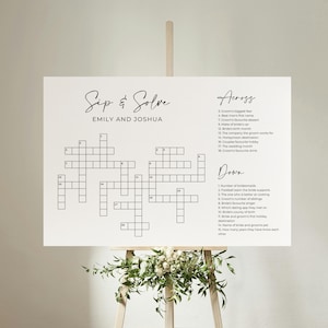 Peut inclure: Un panneau de mots croisés de mariage blanc avec le titre "Sip & Solve" et les noms "Emily et Joshua". Le mot croisé a des indices listés en travers et en bas.