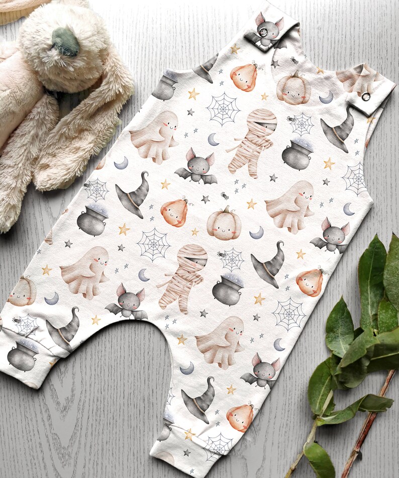 May include: White baby onesie with a Halloween theme. The onesie features a repeating pattern of ghosts, bats, pumpkins, witches hats, cauldrons, and mummies.