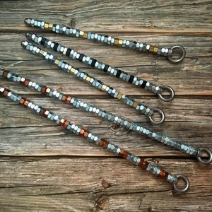 May include: Five silver, gold, and copper beaded necklaces with metal clasps. The necklaces are arranged on a wooden surface.