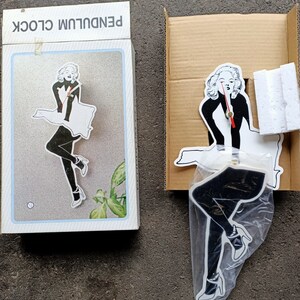 May include: A black and white pendulum clock featuring a silhouette of a woman in a dress and high heels. The clock is packaged in a white box with the words "Pendulum Clock" printed on the front.
